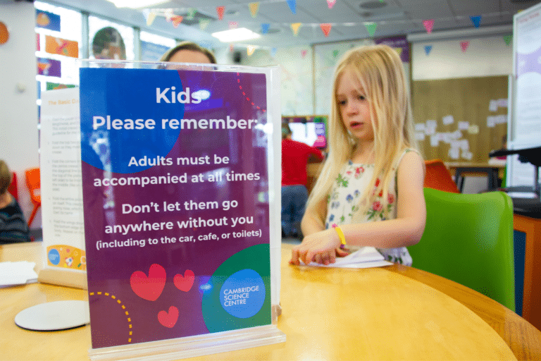 A girl concentrates on making a paper aeroplane with rules for adults in foreground