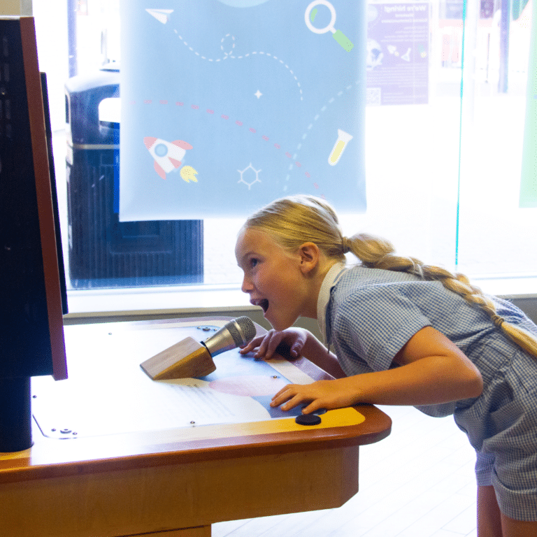 A girl bends down smiling to talk into the sound wave machine