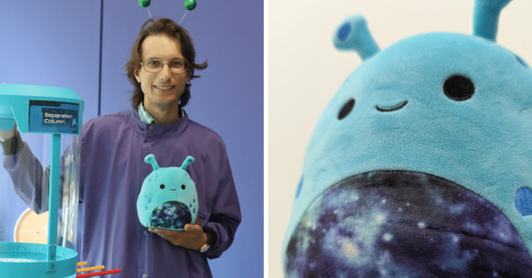 Science Communicator Peter stands with a cute blue stuffed alien toy (a Guarble) and a separation column to his right side