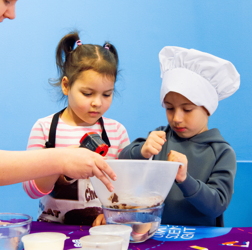 A boy in chefs hat and a girl with a heat monitor as they make chocolate